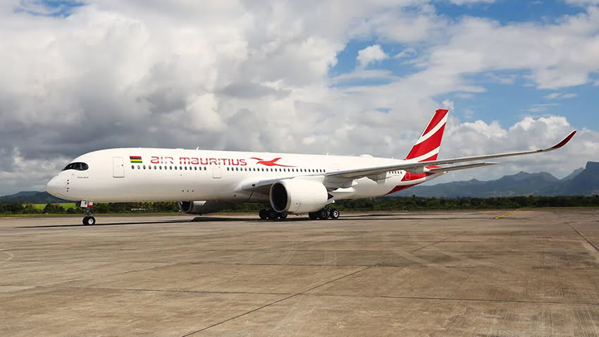 An Air Mauritius aircraft on an airport runway with mountains and a partly cloudy sky in the background