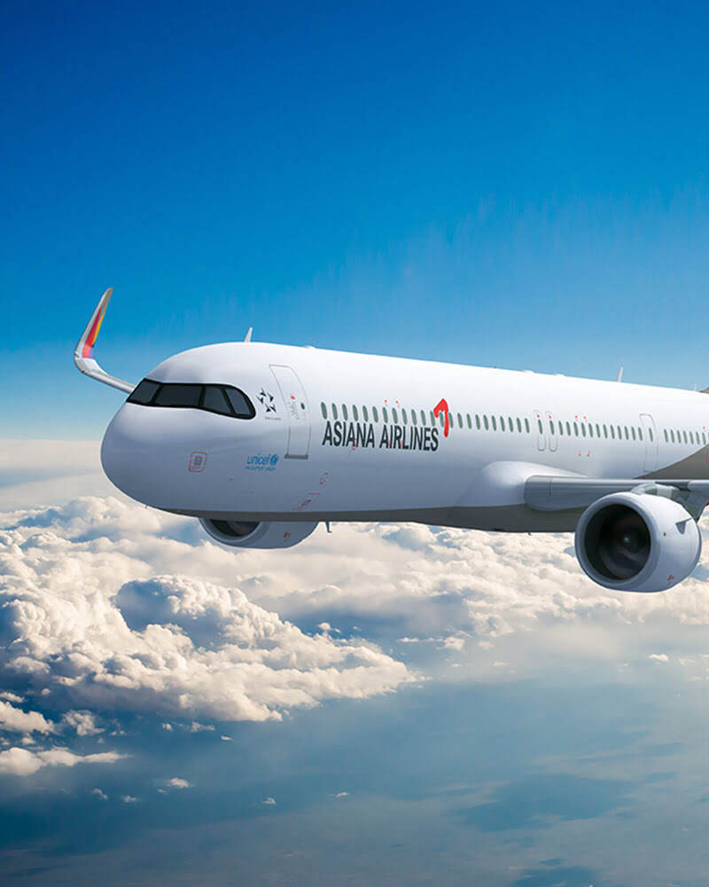 A white Asiana Airlines airplane flying above the clouds with a clear blue sky in the background