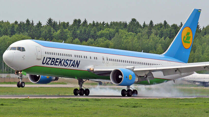 An Uzbekistan Airways aircraft touching down on a runway.