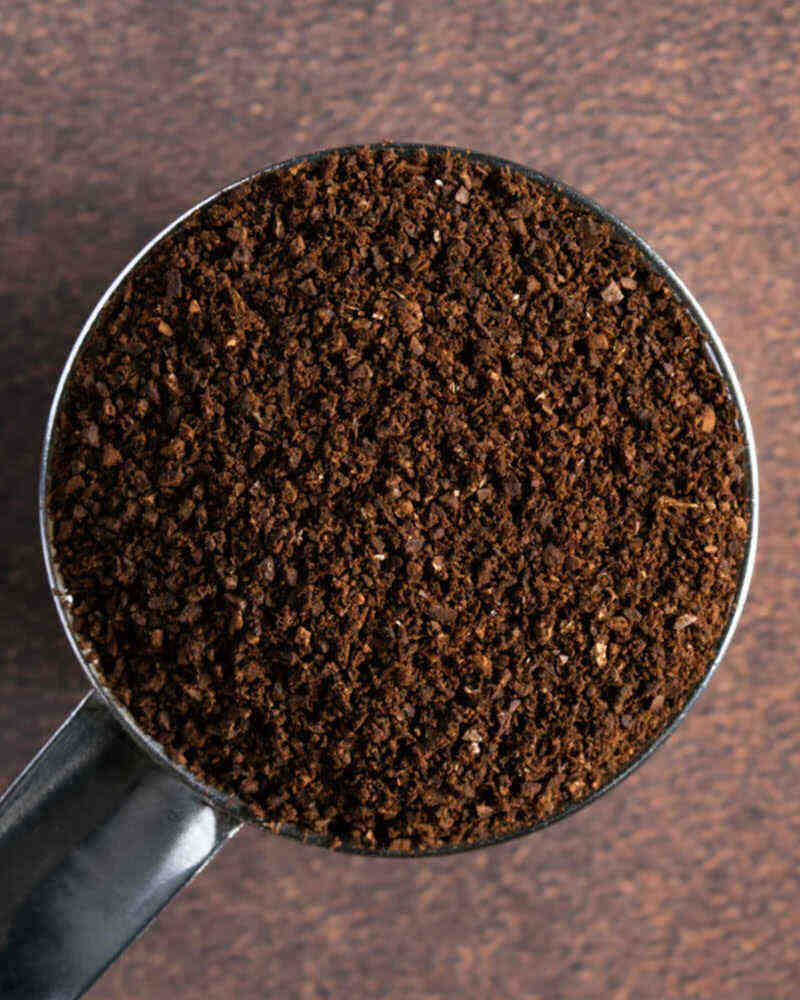 A metal scoop filled with dark brown ground coffee on a textured background