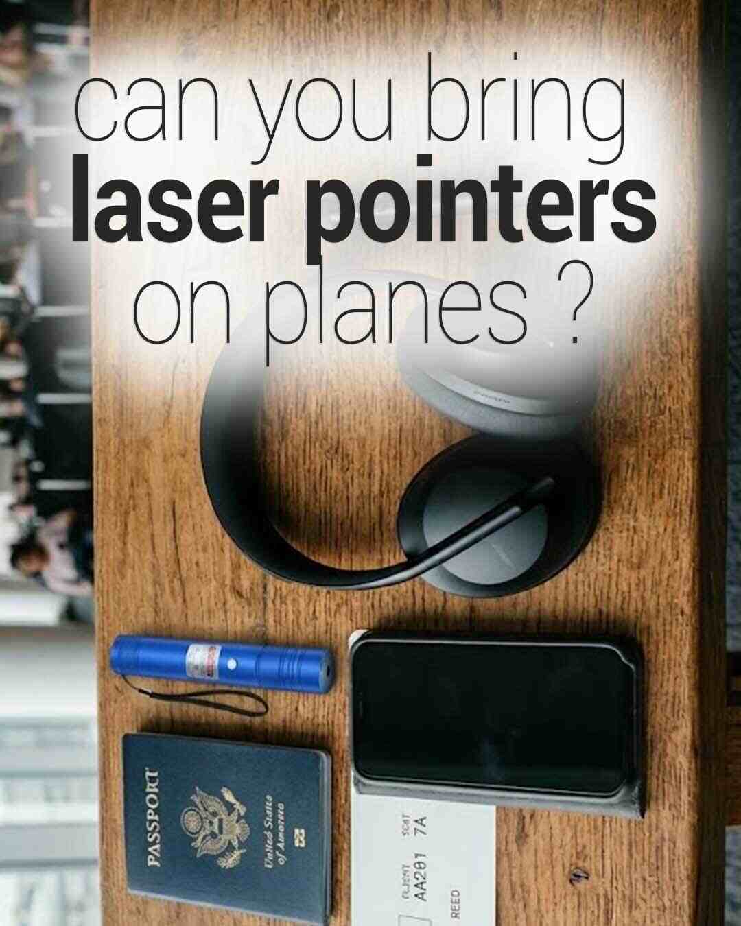 An overhead shot of travel items on a wooden table, featuring a US passport, phone, headphones, and a blue laser pointer, with overlaid text asking, "can you bring laser pointers on planes?"