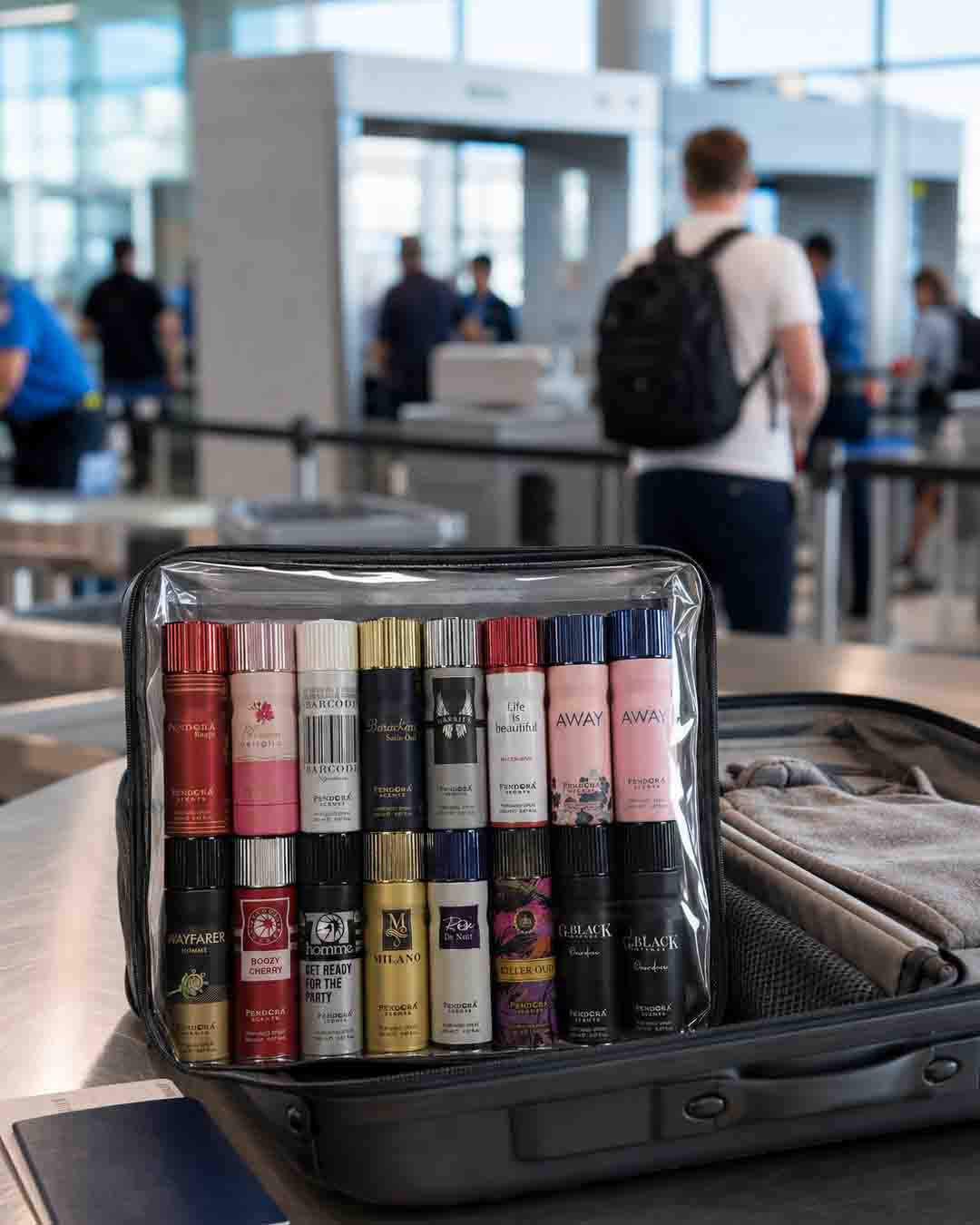 Travel-size body spray cans packed in a clear toiletry bag inside an open suitcase at airport security