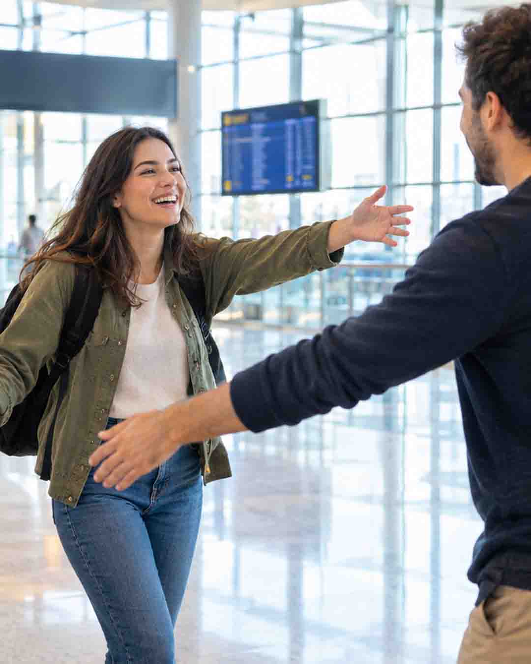 A traveler greets a friend at the airport arrivals hall beside a rolling suitcase