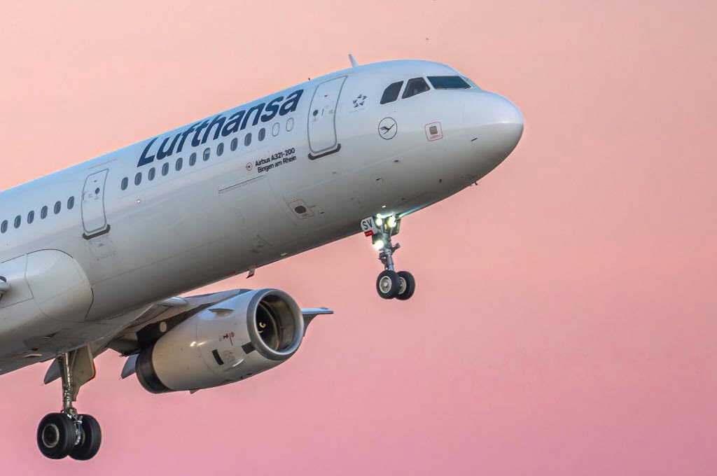 Lufthansa Airbus A321 aircraft taking off at sunset with landing gear extended against a pink sky