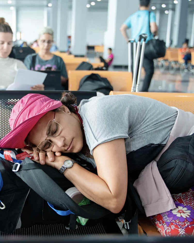 Traveler sleeping on a backpack while waiting for a connecting flight during a long layover at the airport.