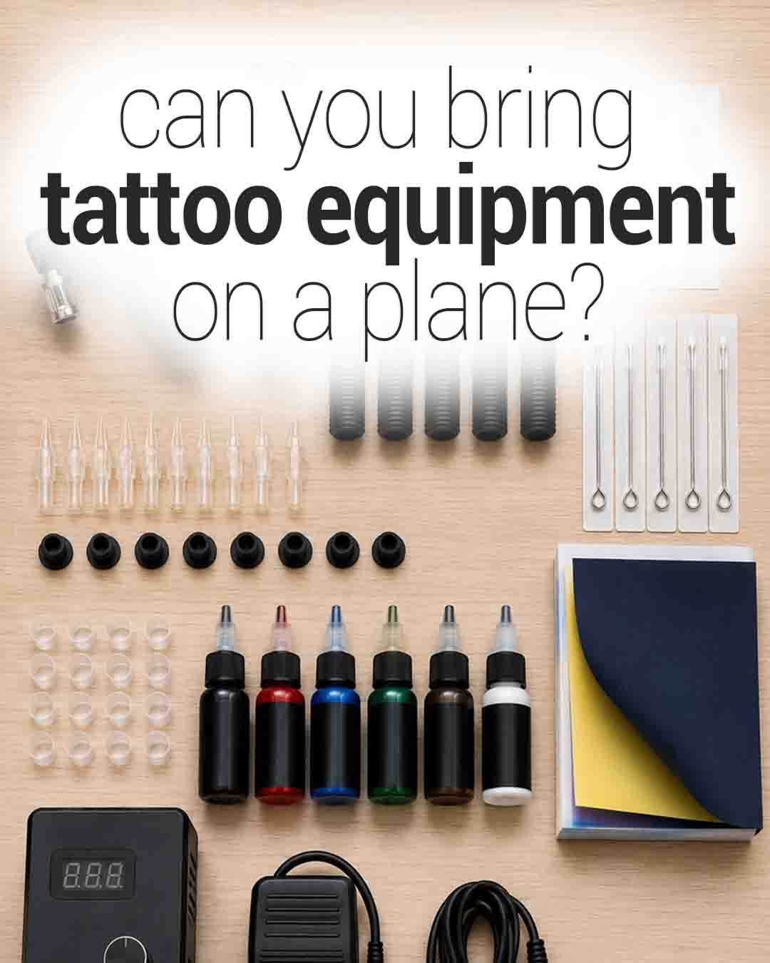 Flat lay of tattoo equipment on a wooden table, including ink bottles, needle cartridges, power supply, and accessories, with the text “Can you bring tattoo equipment on a plane?” displayed at the top
